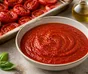 Skål med slät röd tomatsås omgiven av ugnsrostade tomater, vitlök och basilika